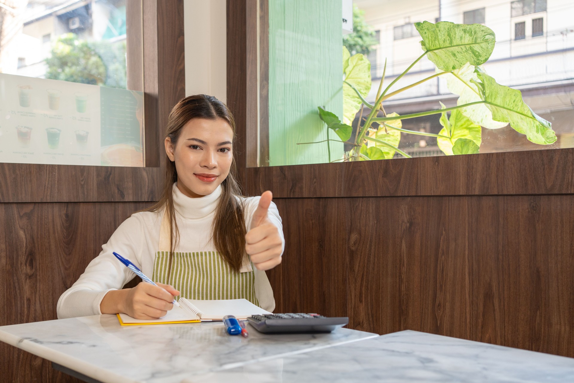 White woman wearing an apron to calculate profit or working on budget for startup owner business. Thumps up success concept.